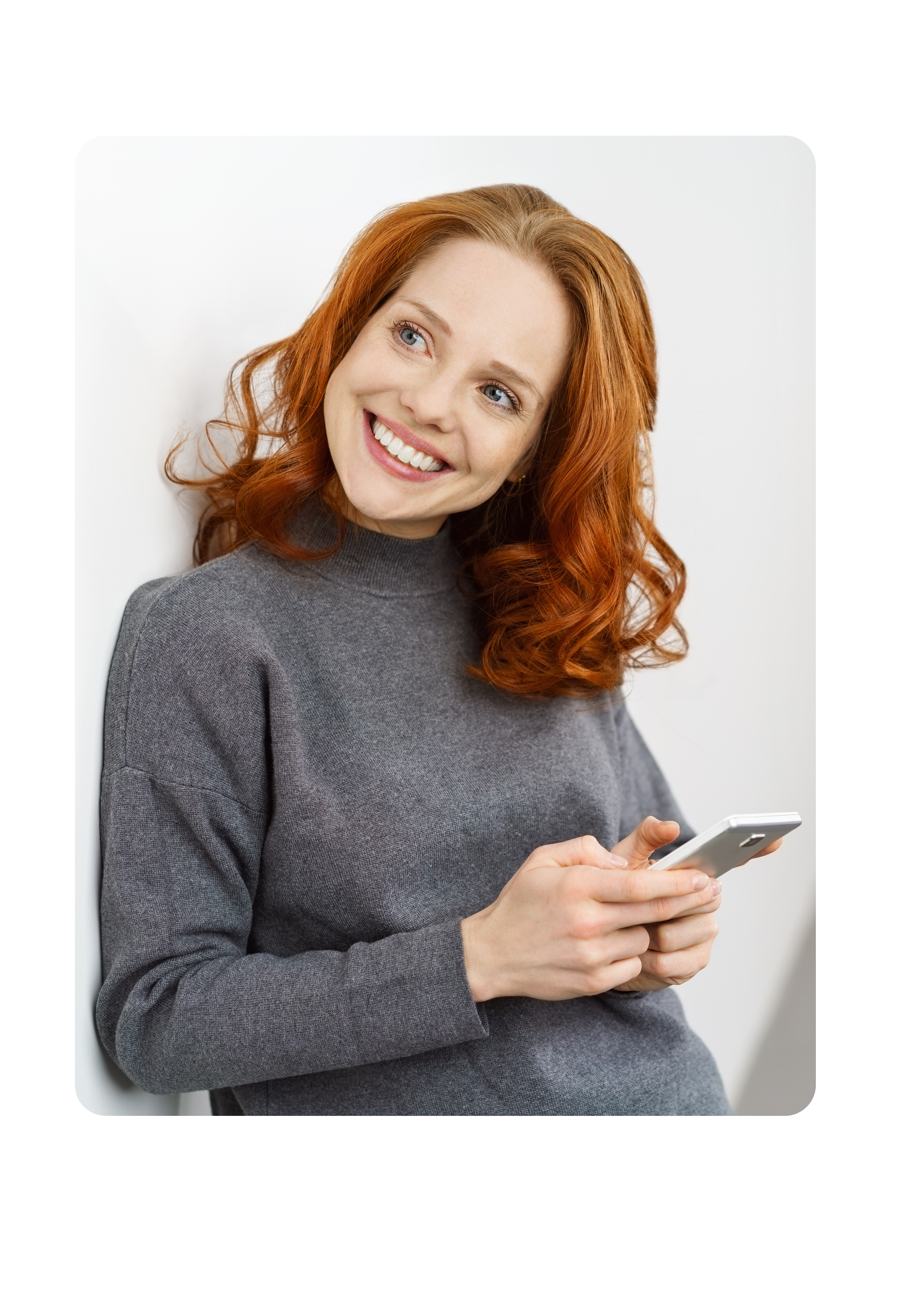 Frau hält Handy und blickt lächelnd in die Ferne.